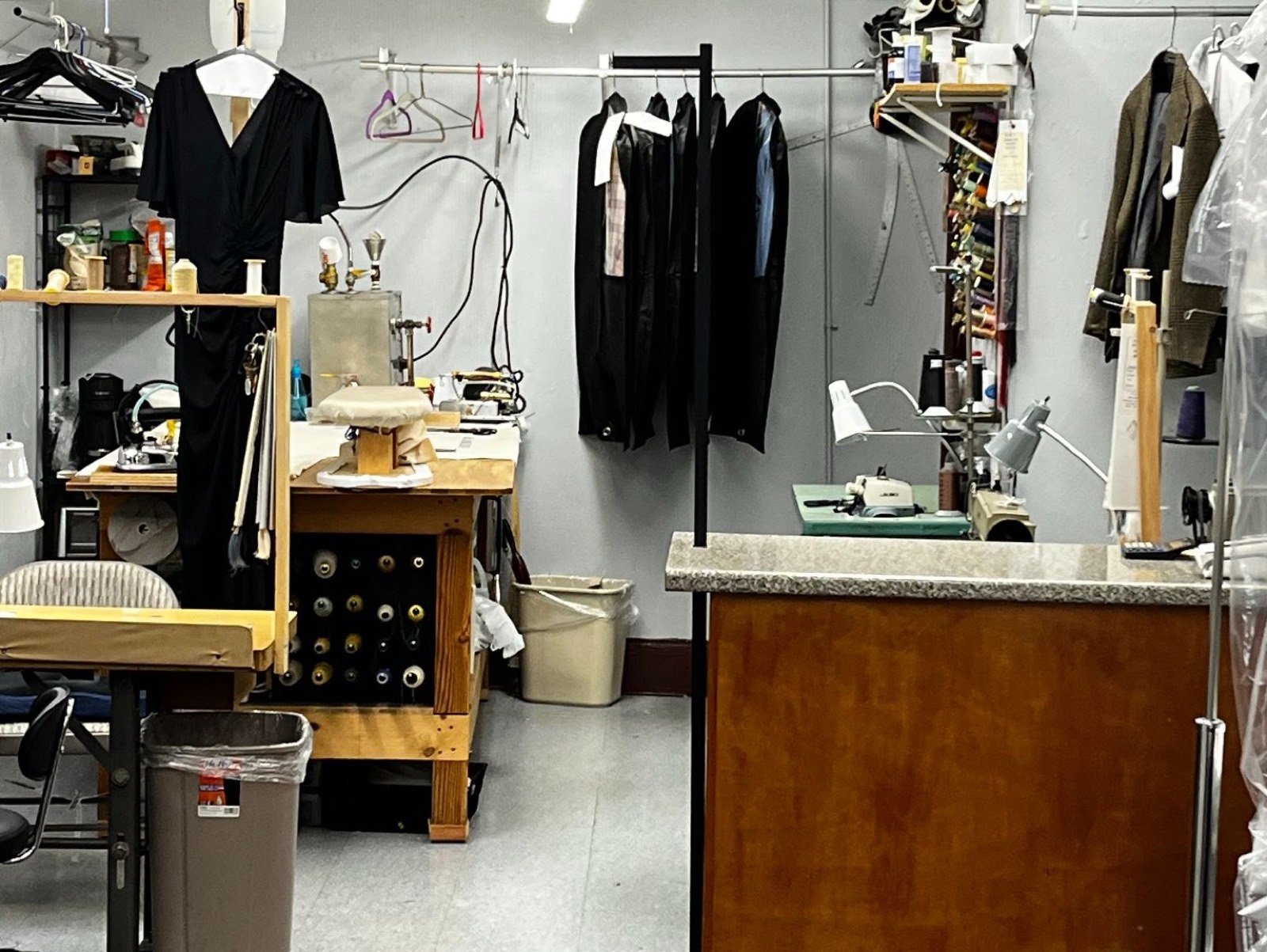 The workroom: sewing machines, thread spools, a pressing station and garments waiting on the rack
